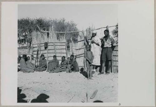 Group of adults and children standing and sitting by their fence
