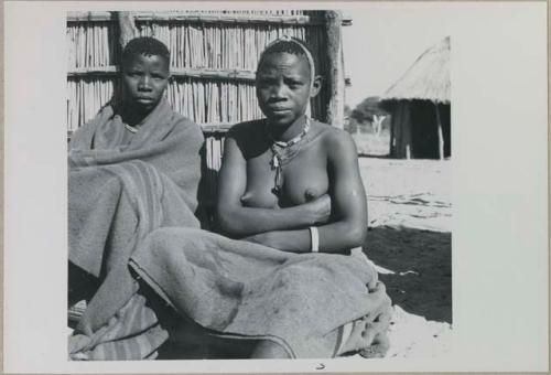 Two women sitting by a fence
