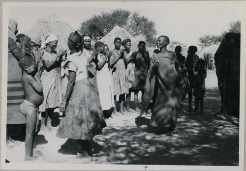 Women dancing in front of a group of women clapping and singing, being recorded
