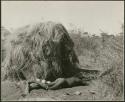 "Living places, shelters": Man sleeping next to a skerm (print is a cropped image)