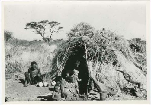 "Living places, shelters": "Old ≠Toma," "Old /Gam" and Khuan//a with /Qui sitting in front of Gau's skerm, with a kudu head lying on the ground next to it (print is a cropped image)