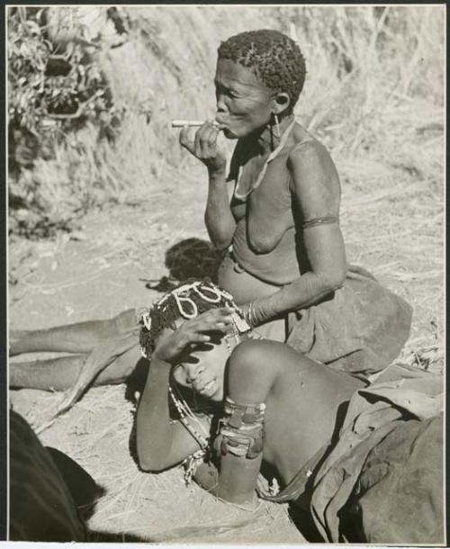 "Smoking": Woman smoking a pipe, with another woman wearing ornaments and upper arm bracelets lying beside her (print is a cropped image)