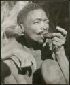 "Smoking": Brother of /Naoka and N!ai (wives of /Ti!kay) smoking a soapstone pipe (print is a cropped image)