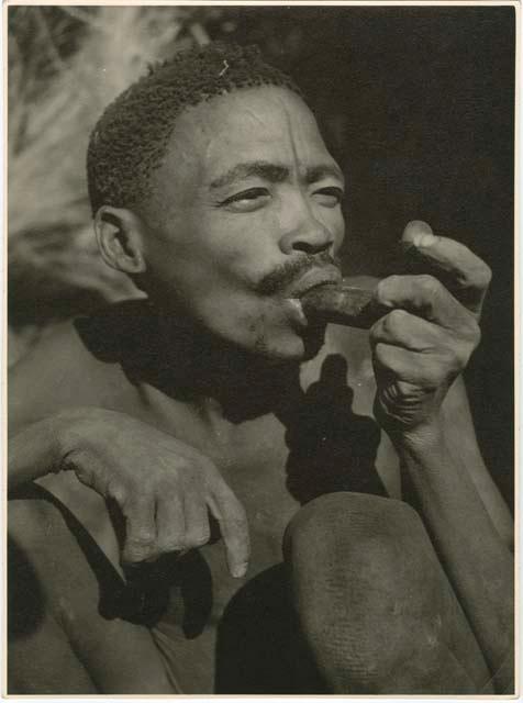 "Smoking": Brother of /Naoka and N!ai (wives of /Ti!kay) smoking a soapstone pipe (print is a cropped image)