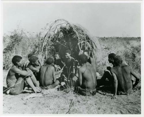 [No folder title]: Group of people sitting in front of a skerm and telling stories, including Zuma (daughter of "Old Xama," wife of Gao), Gao (son of Debe, headman of Band 24 in Cho/ama), and /Qui (brother of "Gao Helmet") (print is a cropped image)