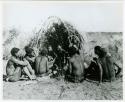 [No folder title]: Group of people sitting in front of a skerm and telling stories, including Zuma (daughter of "Old Xama," wife of Gao), Gao (son of Debe, headman of Band 24 in Cho/ama), and /Qui (brother of "Gao Helmet") (print is a cropped image)