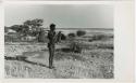 [No folder title]: /Ti!kay carrying bags on a carrying stick and an assegai, with Gautscha Pan in the background (print is a cropped image)