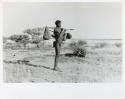[No folder title]: /Ti!kay carrying bags on a carrying stick and an assegai, with Gautscha Pan in the background (print is a cropped image)