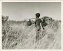 "Water": Boy carrying a water bag made from an animal stomach and another bag on a digging stick on his shoulder, view from behind (print is a cropped image)