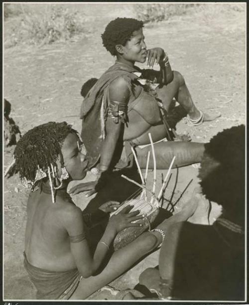 "N!ai in groups": "Little N!ai" playing the //guashi, with Khuan//a (daughter of "Old /Gaishay" and sister of "Gao Medicine") sitting behind her (print is a cropped image)