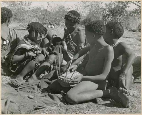 "N!ai in groups": /Gishay (Gau's son) playing the //guashi and sitting with "Little !Nai" and //Khuga
 (print is a cropped image)