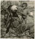 "Children in groups": /Naoka, wife of Ti!kay, drinking from an ostrich eggshell, with !Nani behind her, and /Khoa, her daughter, standing beside her (print is a cropped image)