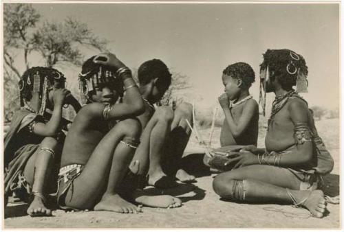 "Children in groups": Girl playing a //guashi, sitting with a group of girls and boys (print is a cropped image)