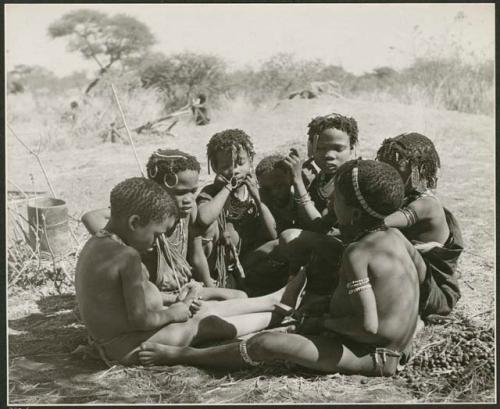 "Children in groups": Group of boys and girls sitting close together, boys are making toy cars (print is a cropped image)