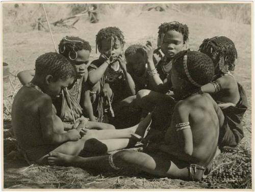 "Children in groups": Group of boys and girls sitting close together, boys are making toy cars (print is a cropped image)