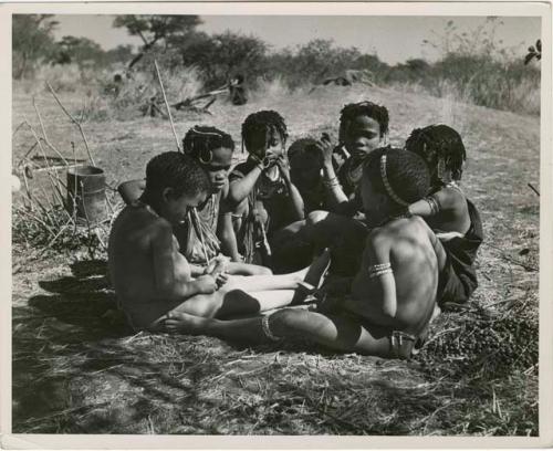 "Children in groups": Group of boys and girls sitting close together, boys are making toy cars (print is a cropped image)