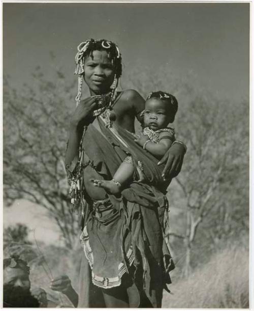 [No folder title]: Woman from /Ti!kay's group standing and carrying her baby (print is a cropped image)