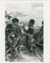 [No folder title]: /Gaishay and an unidentified, young woman helping Debe drink from an ostrich eggshell while Bau watches and another hand steadies Debe; other unidentified people in the background (print is a cropped image)