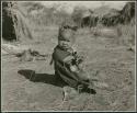 "Carrying children": Khuan//a (daughter of //Ao and ≠Nisa) sitting, wearing ornaments in her hair and a little kaross (print is a cropped image)