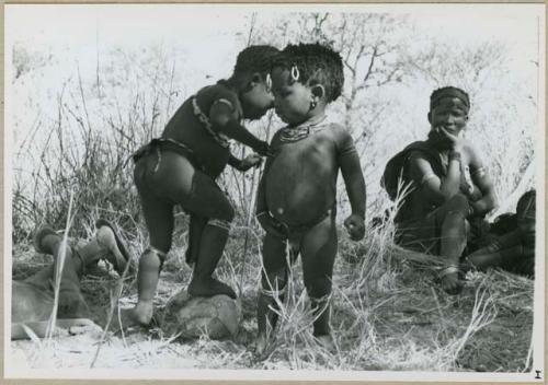 "Carrying children": Two children standing, with women sitting in background (print is a cropped image)