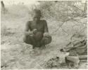 Oukwane squatting in werft while squeezing juice (print is a cropped image)