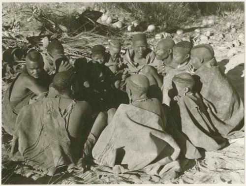 Group of visitors sitting in a cluster, wrapped in karosses (print is a cropped image)