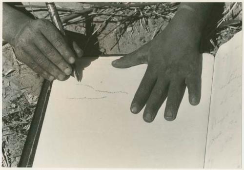 Boy's hand holding a pen and paper displaying marks he created (print is a cropped image)