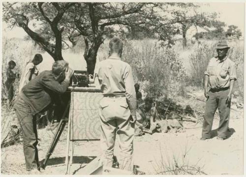 John Marshall setting up sound sync with Daniel Blitz and Wilhelm Camm standing nearby; group of people in the background (print is a cropped image)