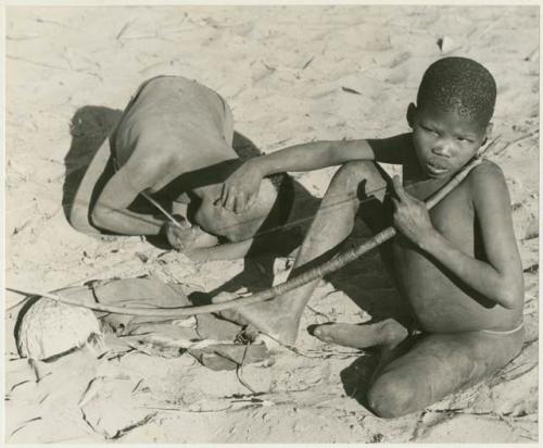 !Oukabe and /Gaiamakwe playing a musical bow together (print is a cropped image)