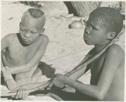 !Oukabe and /Gaiamakwe playing a musical bow together (print is a cropped image)