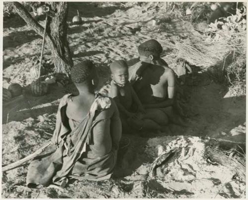 Visiting women and a child sitting by their fire (print is a cropped image)