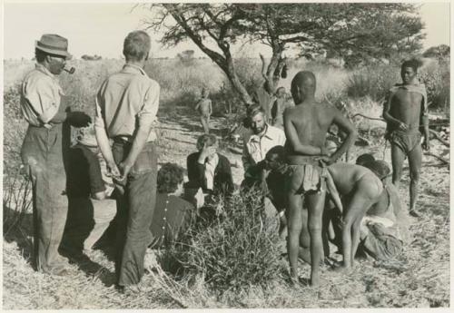 Group of people, including Oukwane and !Gai, being interviewed by Lorna Marshall and Elizabeth Marshall, with Casper Kruger, Kernel Ledimo, Wilhelm Camm, John Marshall, and Daniel Blitz watching (print is a cropped image)