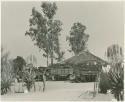 Expedition's trucks off-loading at one of its camps beside a hut, seen from a distance (print is a cropped image)