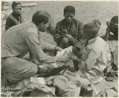 William Donnellan bandaging "/Qui Hunter's" leg, with ≠Toma and other people present (print is a cropped image)