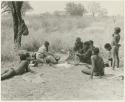 "/Qui Hunter" and ≠Toma sitting with other Ju/'hoansi, seen from a distance (print is a cropped image)