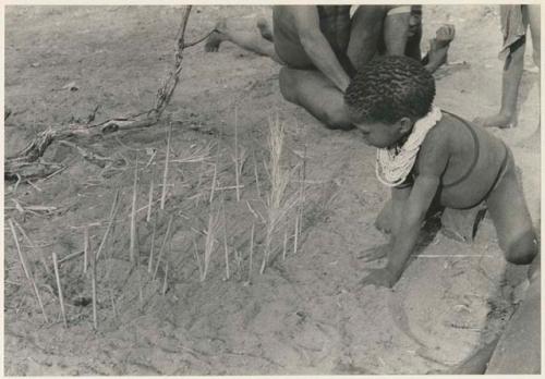 Boy looking at the sticks for constructing a playhouse (print is a cropped image)