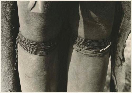 Person's legs with beads worn by Ju/'hoan women below their knee and a thong bracelet (print is a cropped image)