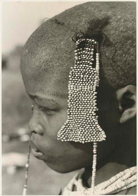 Close-up of bead accessory hanging from tuft of hair of a visiting girl (print is a cropped image; image is flipped)