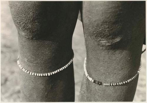 Bead bracelets under a person's knees (print is a cropped image)