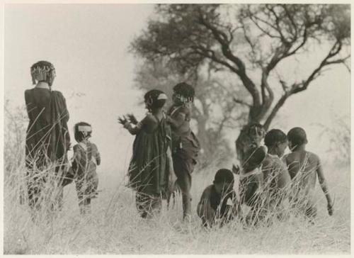 Boys dancing and girls clapping, seen from the back (print is a cropped image)