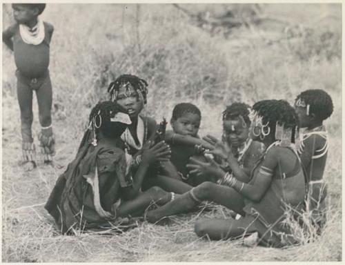 Girls sitting in a circle, clapping and singing, and another child standing in the background