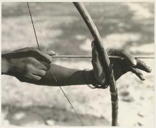 Close-up of "Crooked /Qui's" hands, showing arrow release and position of left hand on bow (print is a cropped image)