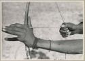 Close-up of "Crooked /Qui's" hands, showing arrow release and position of left hand on bow (print is a cropped image)