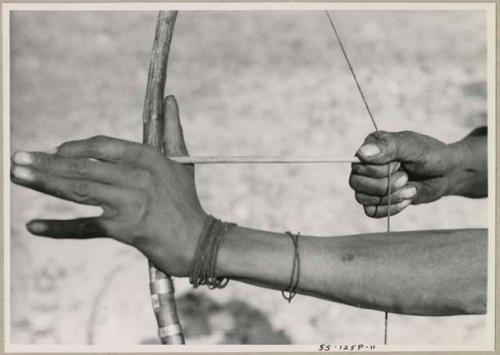 Close-up of "Crooked /Qui's" hands, showing arrow release and position of left hand on bow (print is a cropped image)