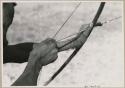 Close-up of "Crooked /Qui's" hands, showing arrow release and position of left hand on bow (print is a cropped image)