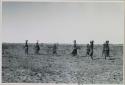 Group of women walking in a line, carrying buckets on top of their heads
