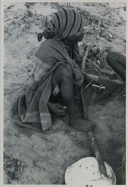 Woman sitting and playing a dandiri, seen from behind
