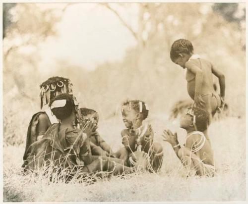 "Children playing curing dance": Girls clapping and singing, with a little boy dancing (print is a cropped image)