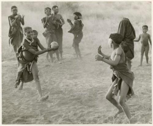 "Women's Ball Game": Girls playing N!owa t/ama (melon tossing game) / tamah n!o’an (ball game); an unidentified, visiting girl catches the melon while other children watch in the background (print is a cropped image)