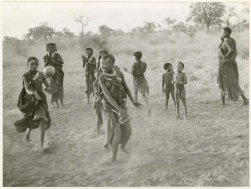 "Women's Ball Game": Girls playing N!owa t/ama (melon tossing game) / tamah n!o’an (ball game); !Ungka's cousin catches the ball from an unidentified, visiting girl while other children watch in the background (print is a cropped image)